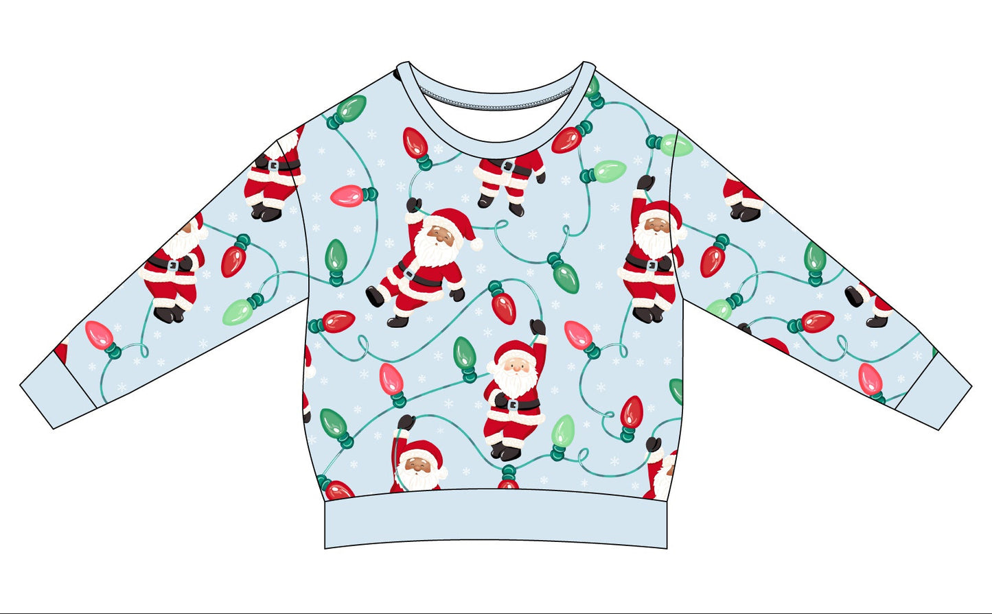 A flat-lay illustration of a long-sleeve crewneck sweatshirt shown from both the front and back views. The sweatshirt has a light blue base color with a festive Christmas print featuring Santa Claus, reindeer, and red holiday lights.