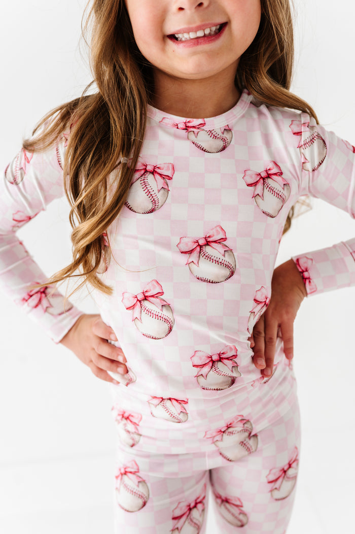 Child wearing a pajama set with baseball and bow pattern on a white background