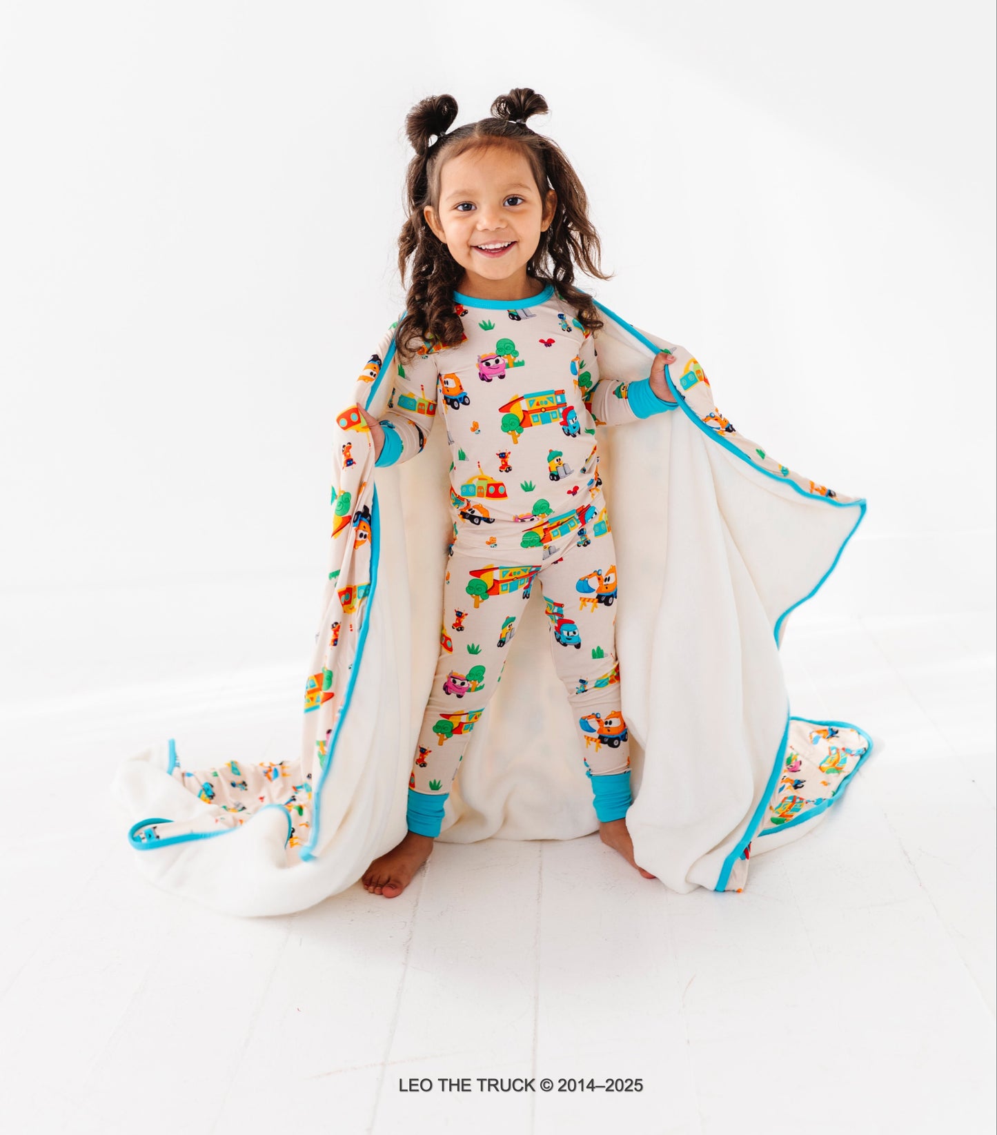 Little girl wearing colorful Leo the Truck bamboo pajamas on a white background
