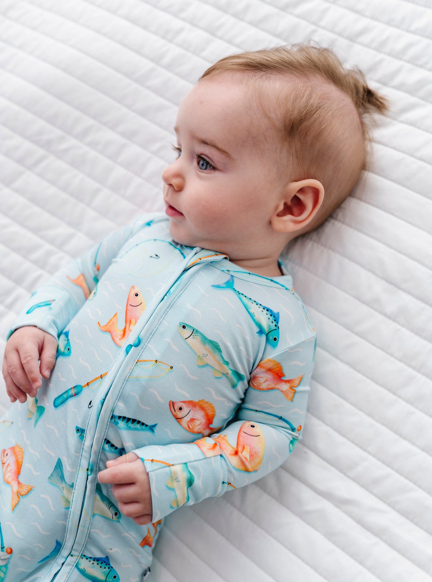 Baby wearing a romper with fish pattern lying on a textured white surface