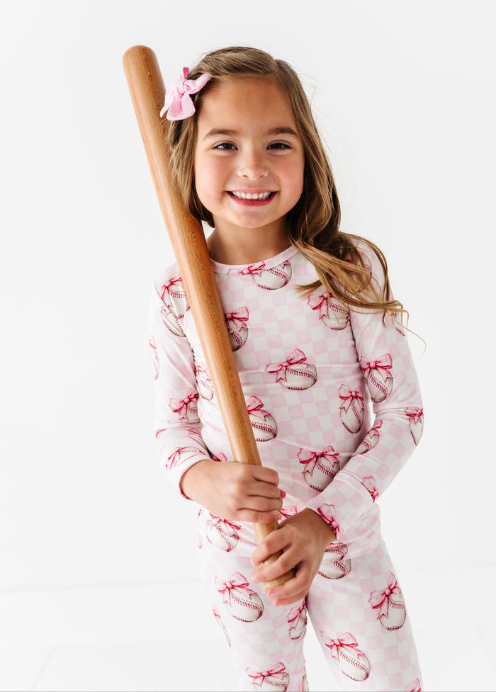Young girl in bamboo pajamas holding a baseball bat on a white background