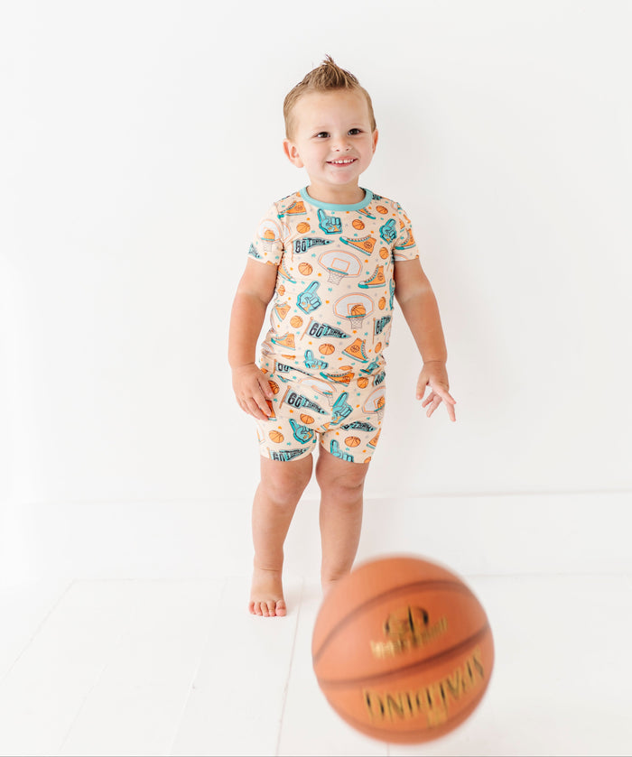 Child wearing a bamboo onesie with sports-themed design, standing next to a basketball on a white background