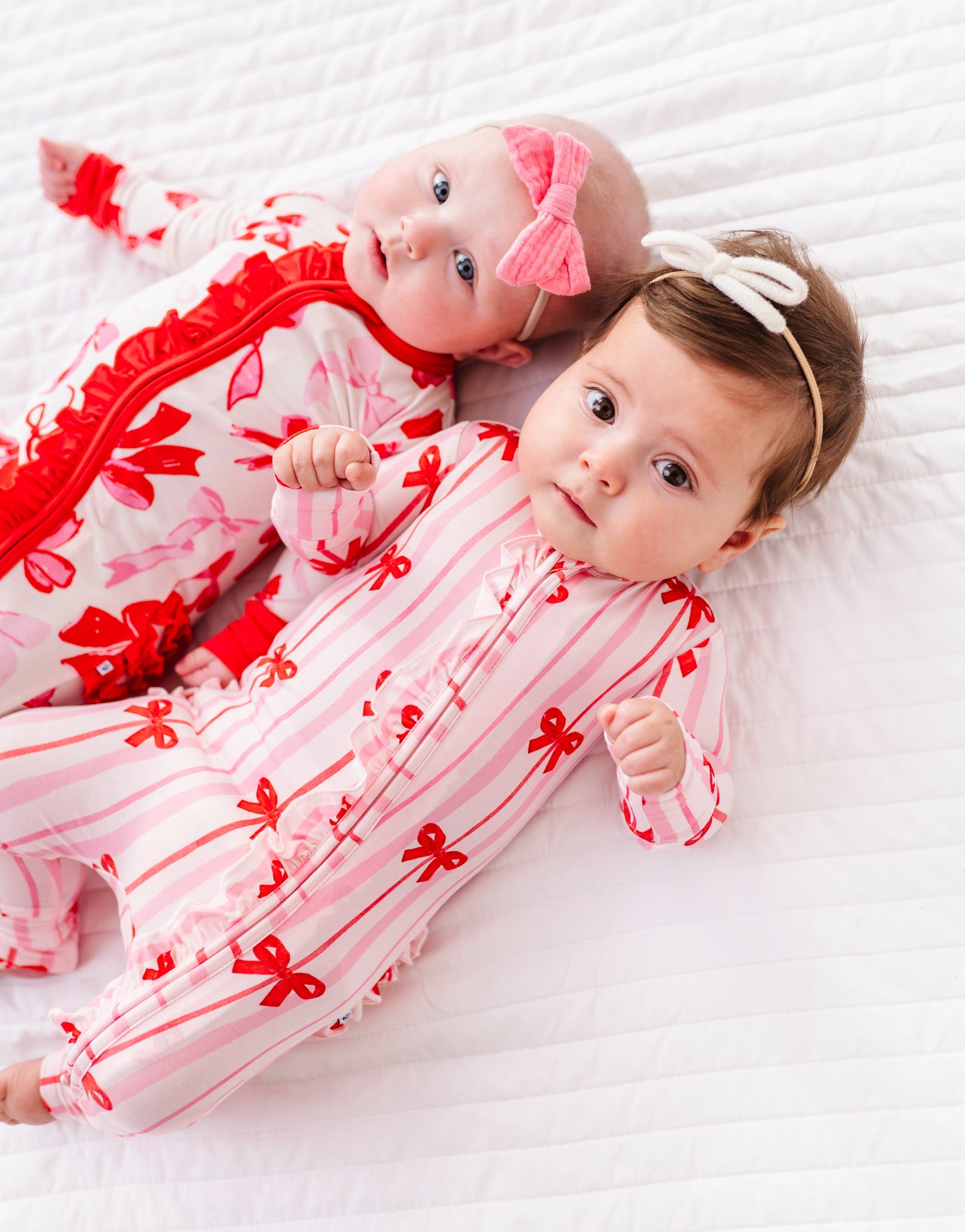 Two babies wearing coordinating Birdie Bean bamboo rompers with ribbon prints