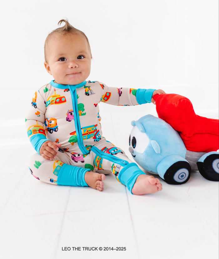 Baby in a colorful Leo the Truck bamboo convertible romper playing with a Leo the Truck plush toy on a white background