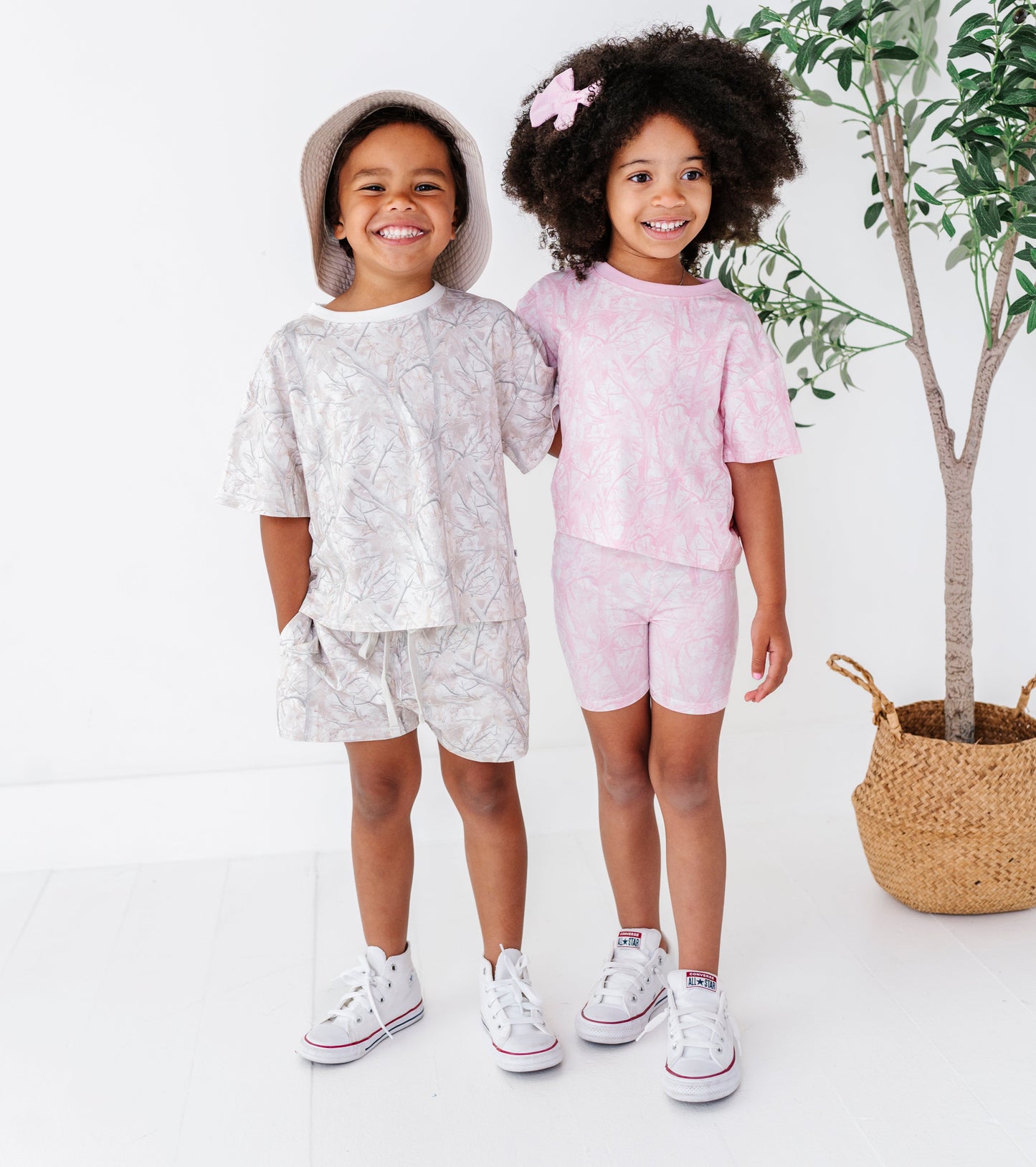 Two children in matching outfits standing next to a plant on a white background