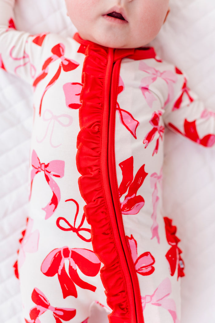 Close-up of pink bamboo baby romper with red bow print and front ruffle detail
