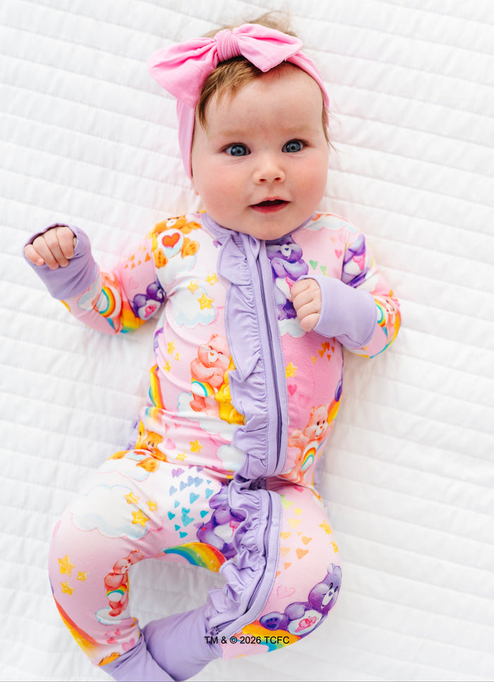 Baby wearing a bamboo Care Bears™ convertible romper with rainbow patterns on a white background