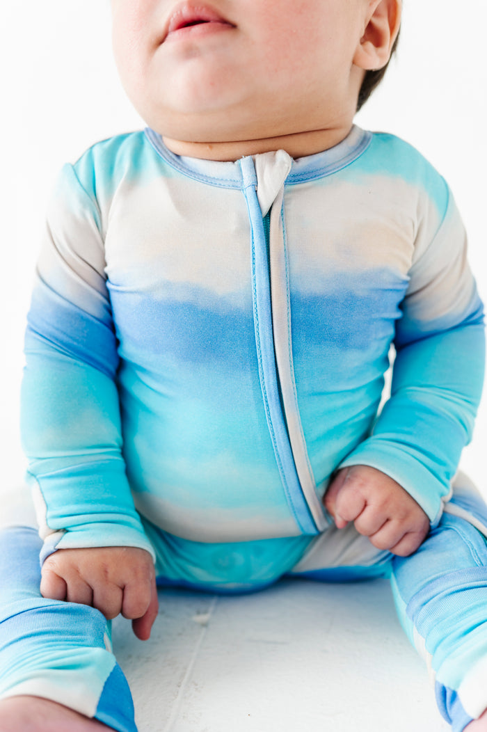 Baby wearing a blue and white gradient bamboo convertible romper on a white background