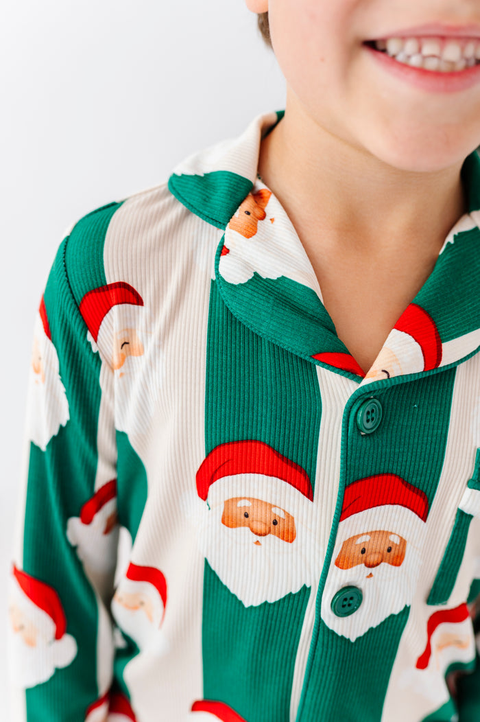 A close-up of a child wearing green and white striped bamboo pajamas with a Santa Claus face print, showing the collar, buttons, and part of the smiling face against a plain light background.