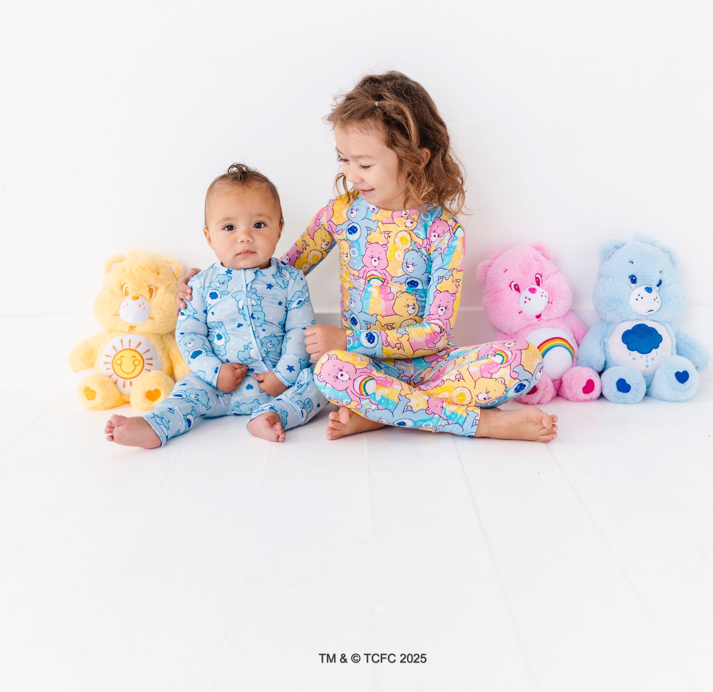 Toddler sitting in Care Bears™ Stare bamboo pajamas styled with matching Care Bears plush toys