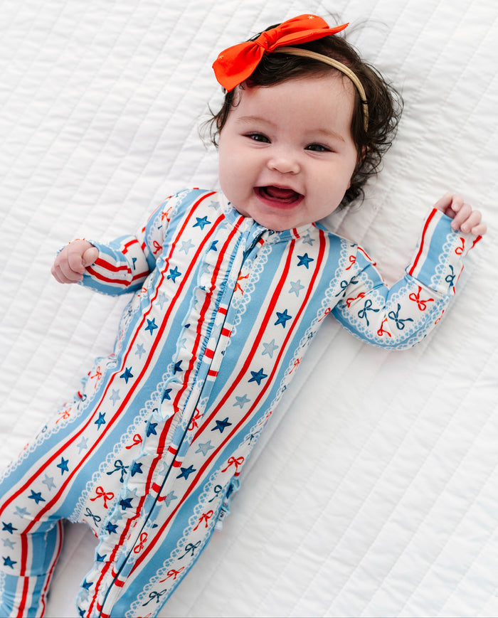 Baby wearing a colorful bamboo convertible romper with stars and stripes, lying on a white textured surface.