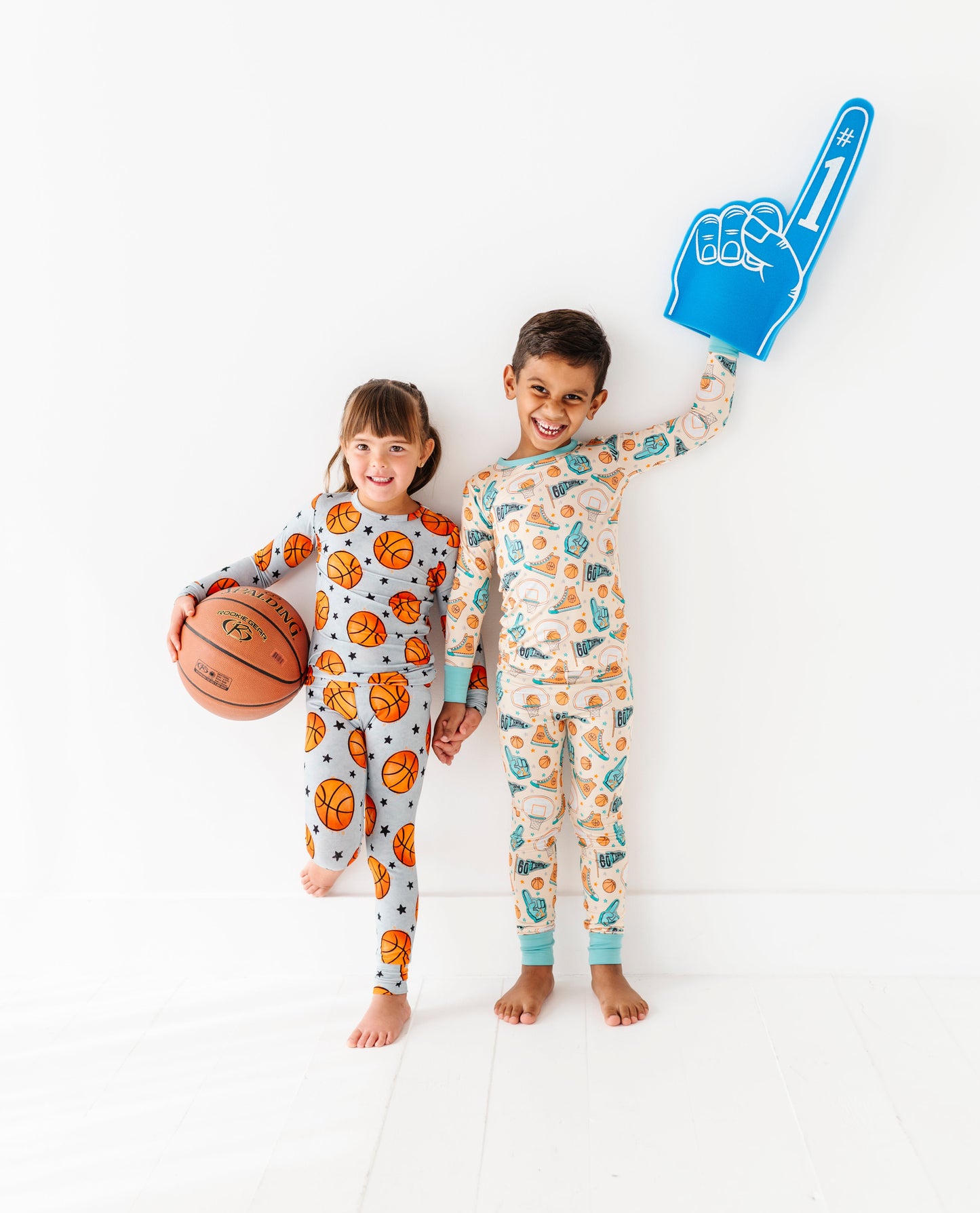 Two children in basketball bamboo pajamas holding a basketball and foam hand on a white background