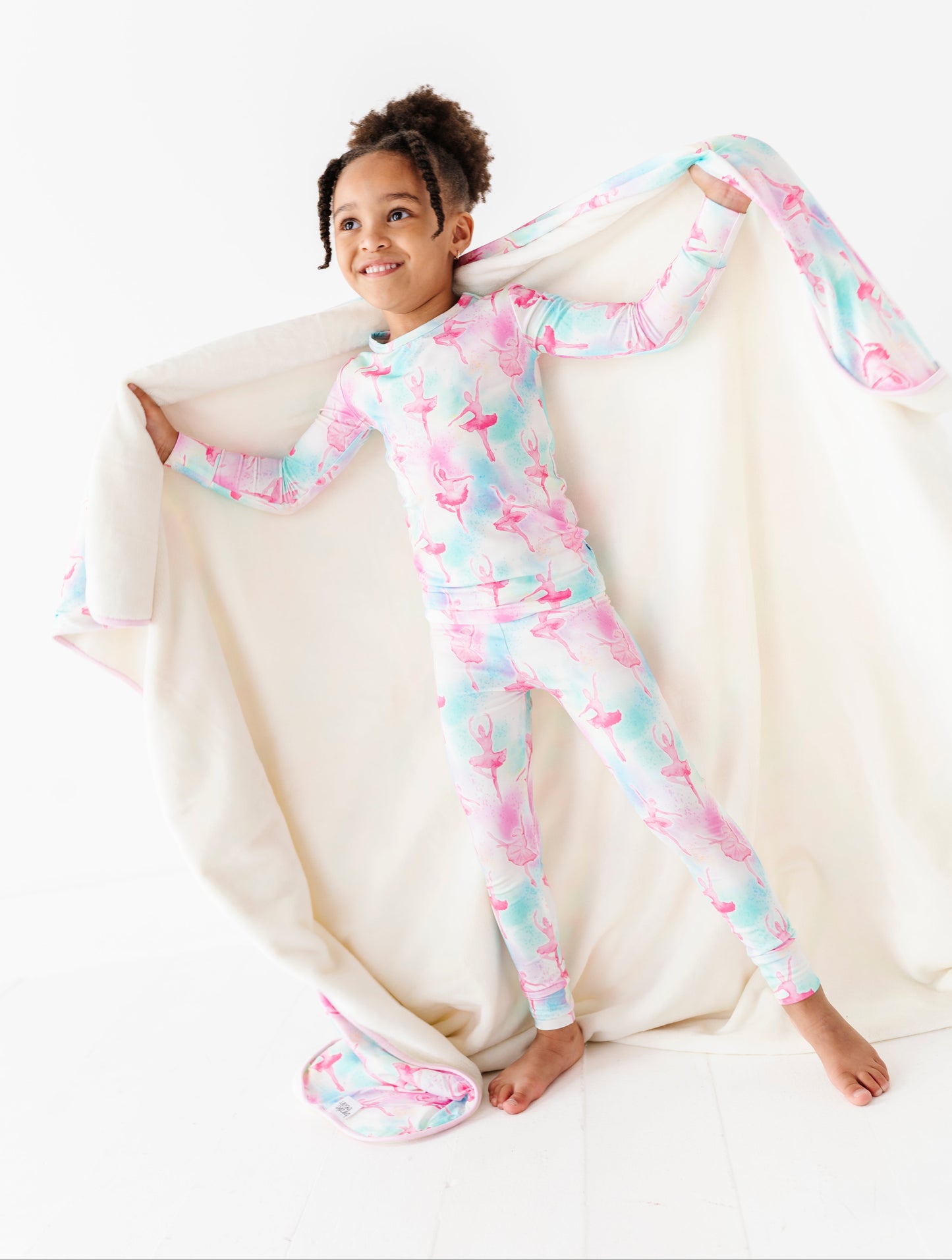 Child wearing a colorful ballet-themed bamboo pajamas, sitting on a white surface with a bamboo plush blanket.