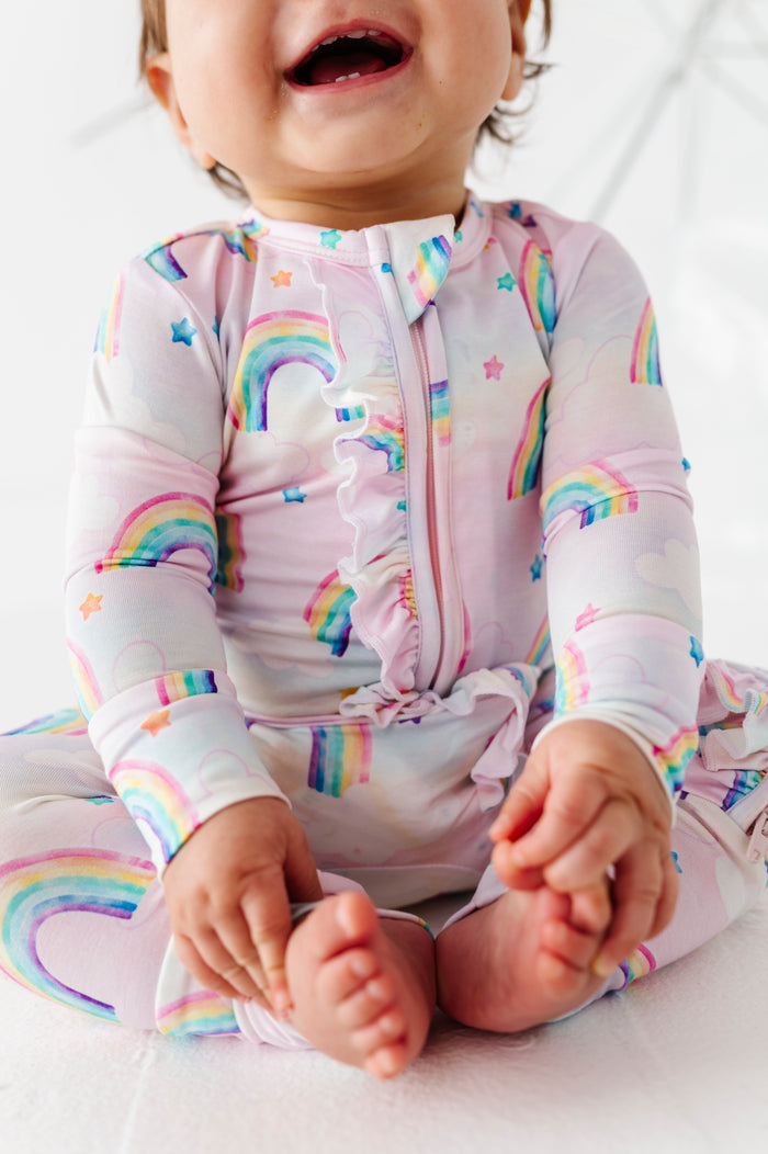 Child wearing a colorful watercolor rainbow-themed bamboo convertible romper on a white background