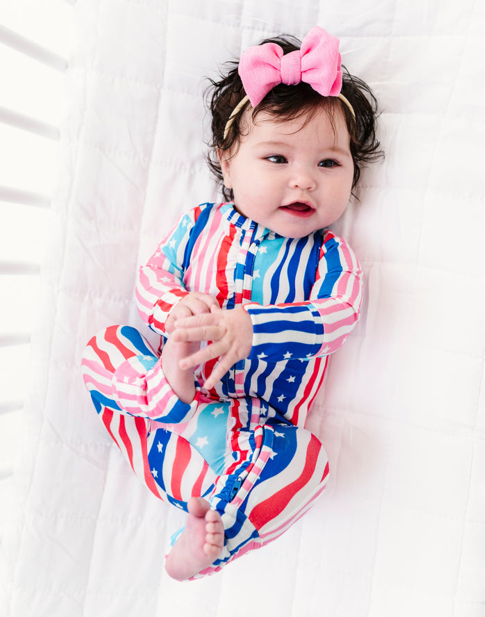 Baby wearing a colorful striped bamboo convertible romper with a pink bow on a white background