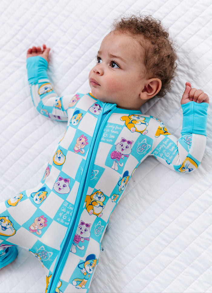 Baby wearing a blue and white 44 Cats patterned convertible romper lying on a white bed