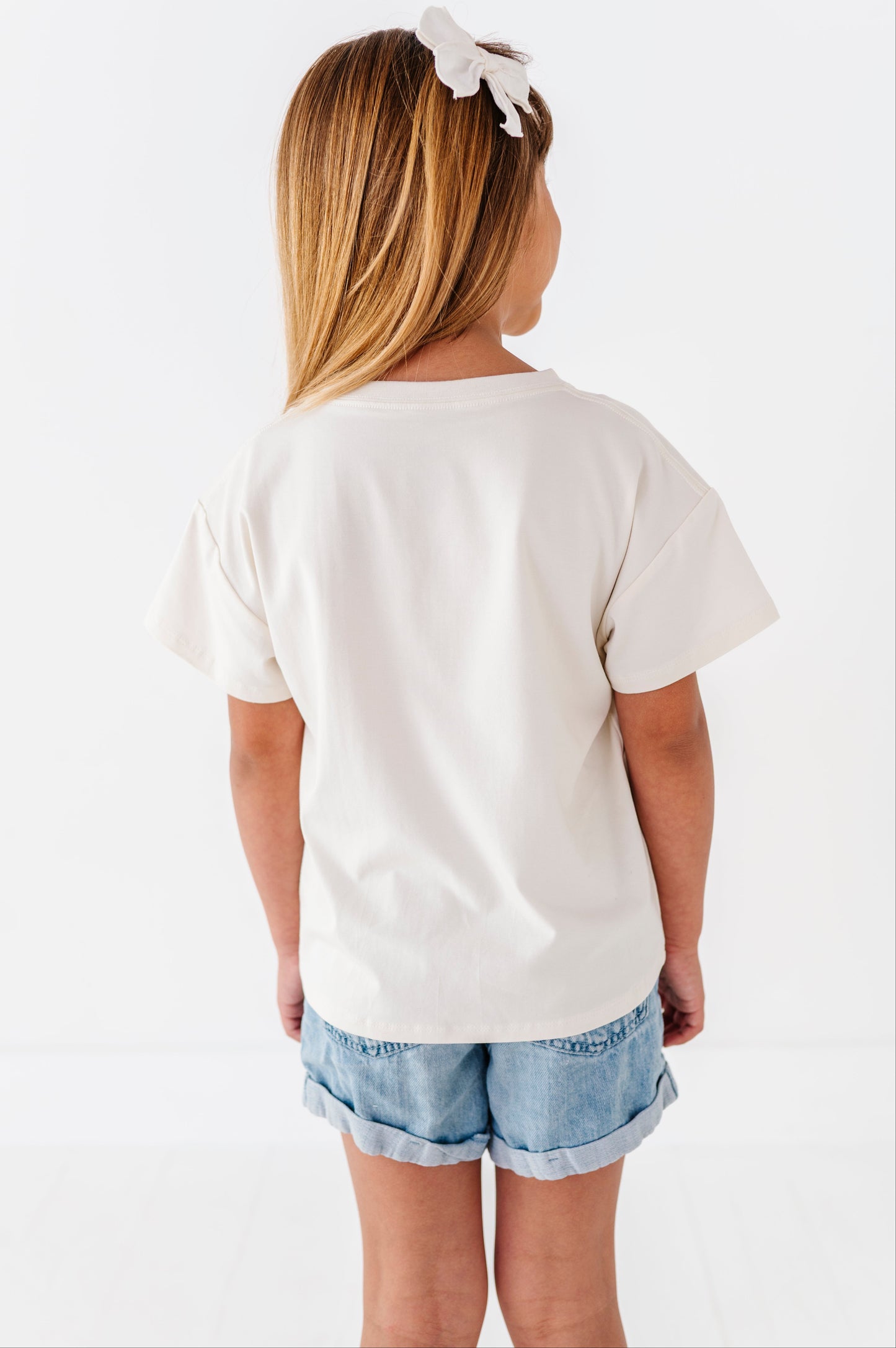 Young girl wearing a white t-shirt and denim shorts on a white background
