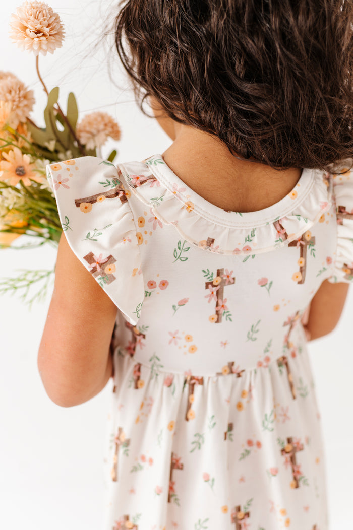 Child wearing a floral Easter dress holding flowers, with a focus on the dress and child's back.