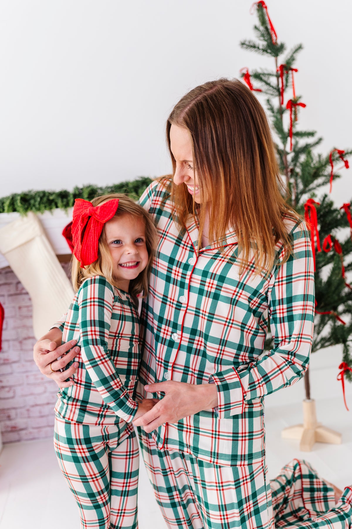 A mom and daughter standing in front of a Christmas tree wearing classic red-and-green plaid matching bamboo pajamas