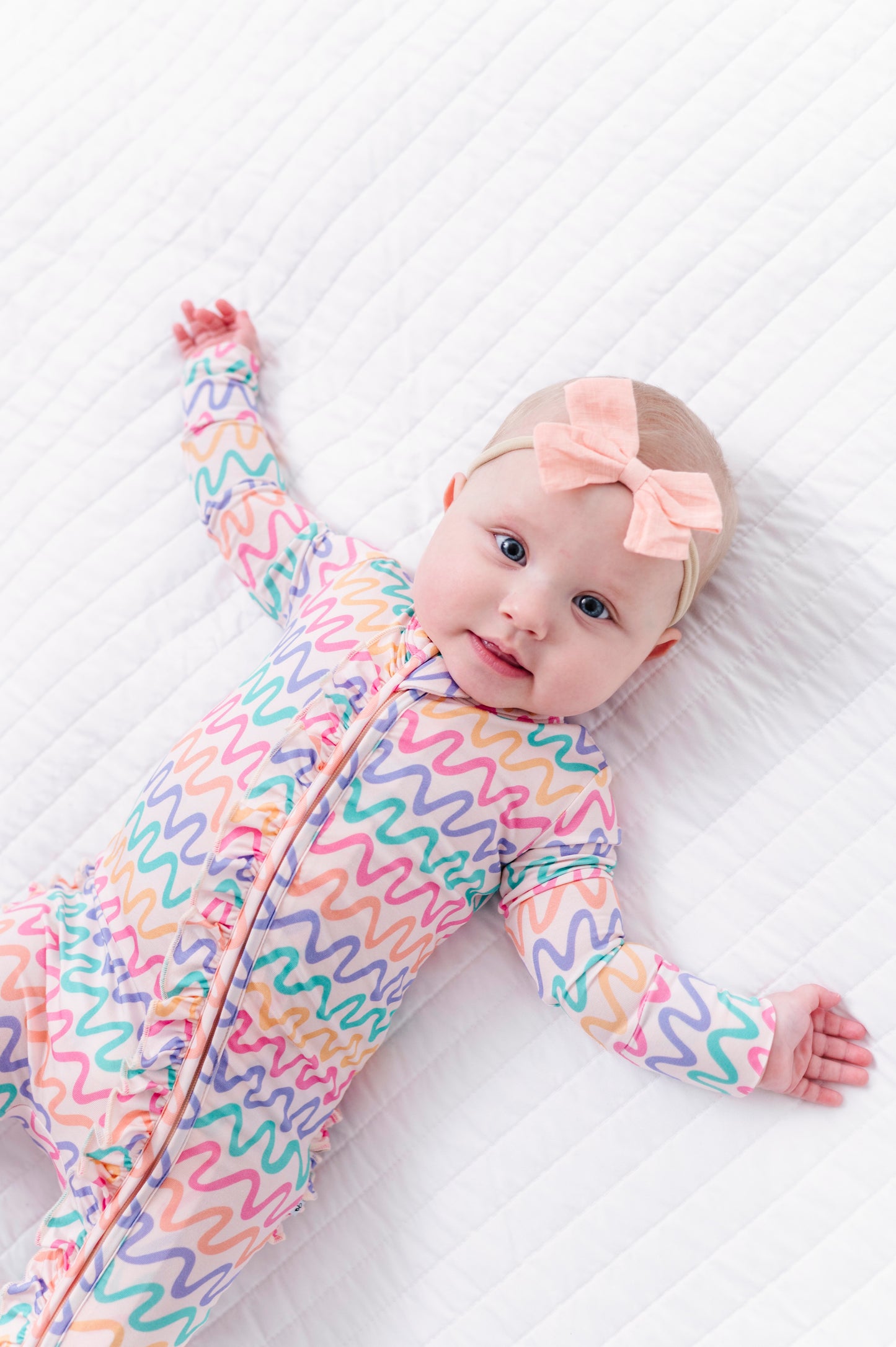 Baby wearing a colorful bamboo convertible romper with a pink bow on a white background