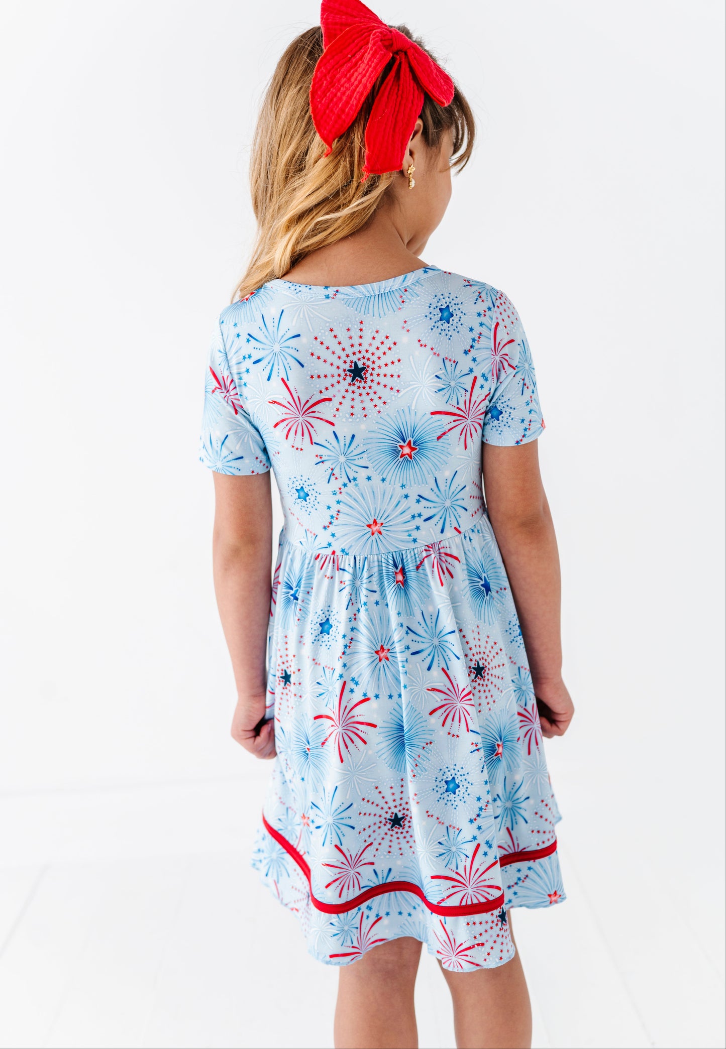 Child wearing a light blue bamboo dress with red and white firework patterns on a white background