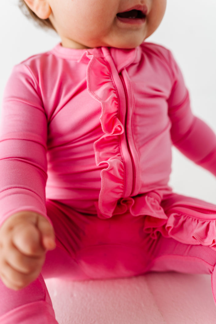 Baby wearing a pink bamboo romper with ruffles on a white background