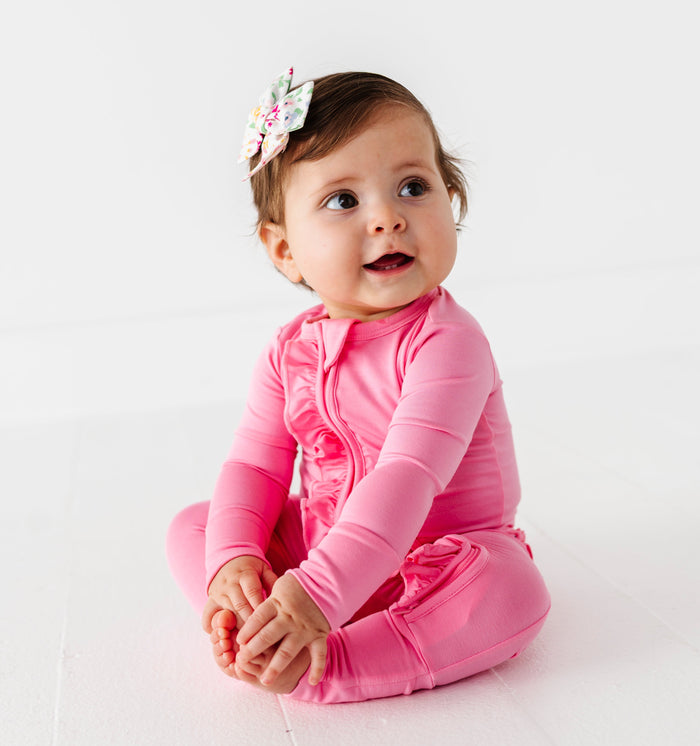 Baby in a bright pink bamboo zip romper on a white background