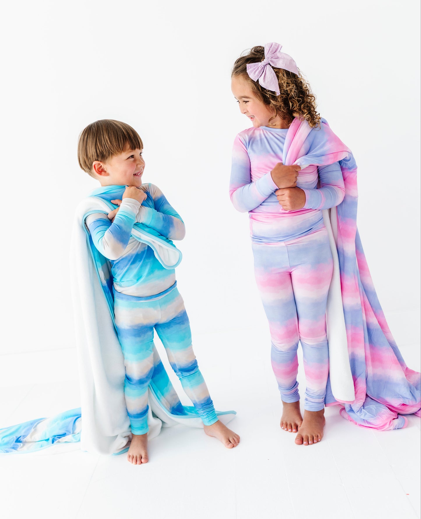 Two children wearing colorful striped pajamas and blankets on a white background