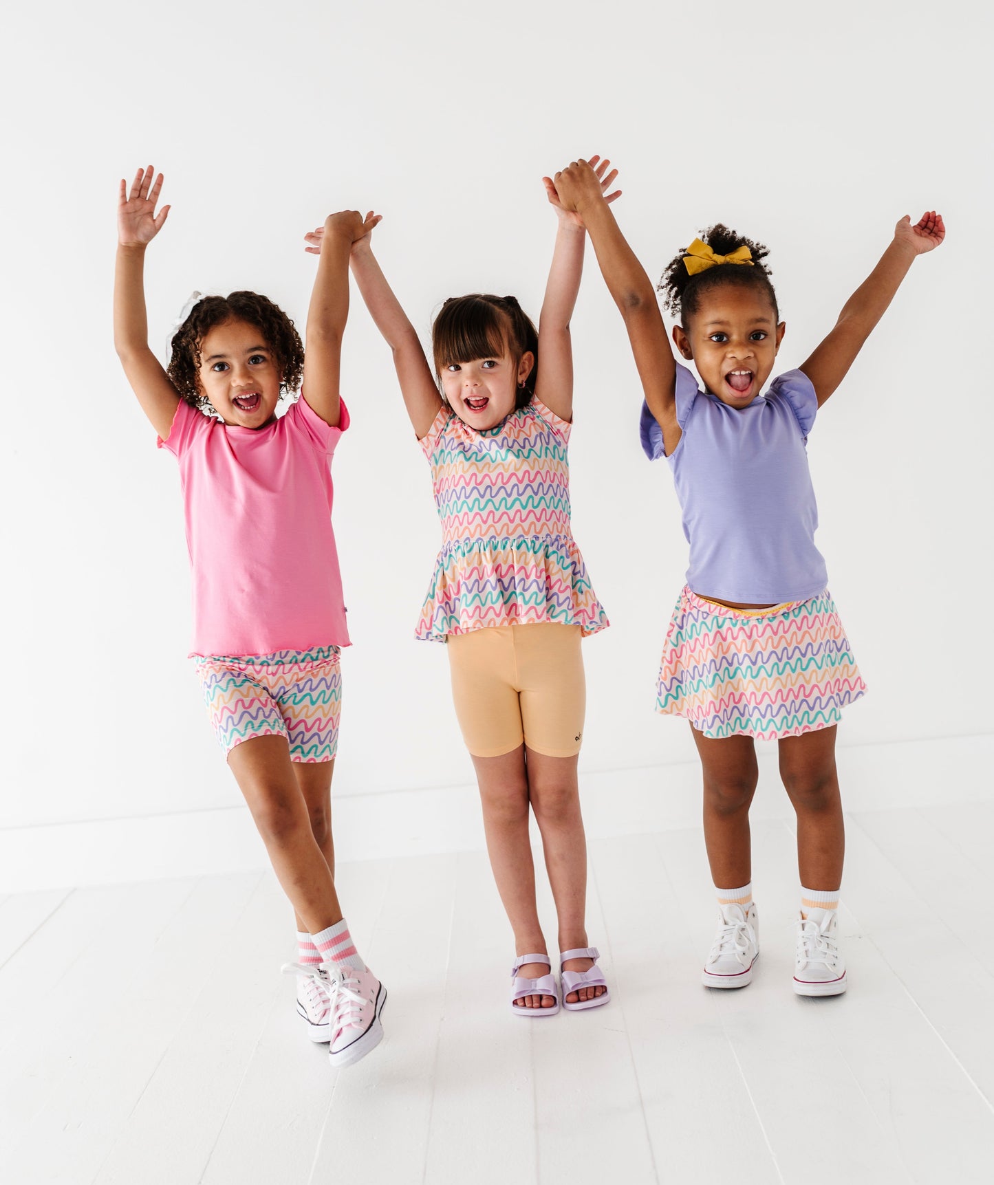 Three children in colorful bamboo outfits with arms raised against a white background