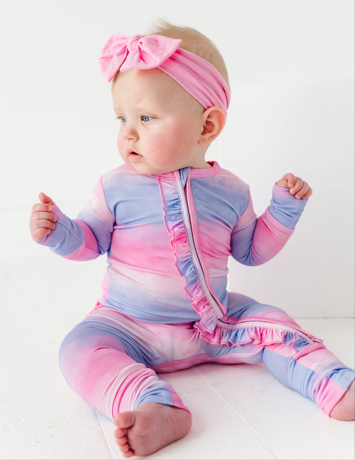 Baby in a colorful bamboo zip romper with a pink headband on a white background