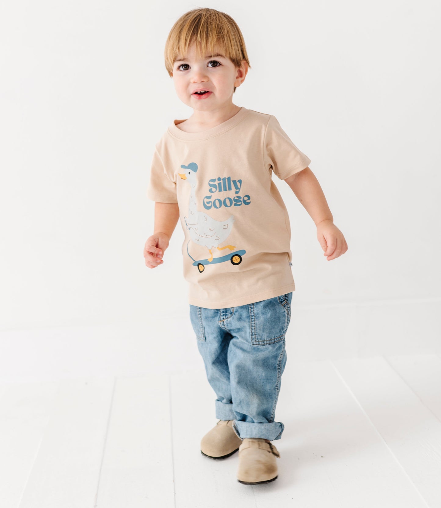 Child wearing a beige t-shirt with silly goose wording and a goose on a scooter on a white background
