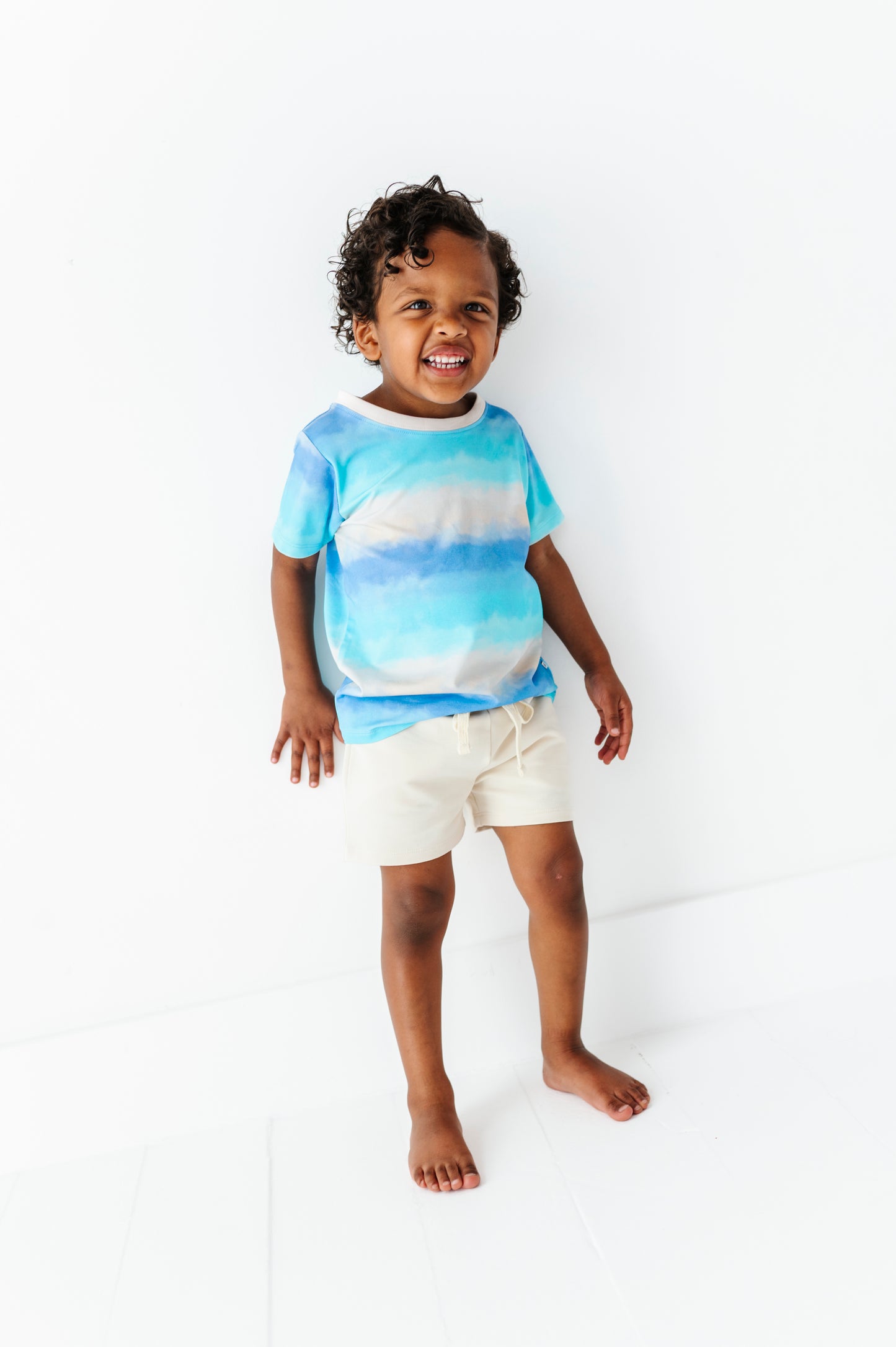 Child wearing a blue and white ombre bamboo-cotton shirt and beige shorts on a white background