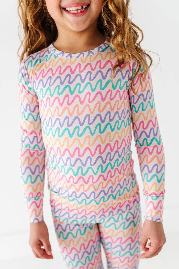 Child wearing a colorful wavy pattern bamboo pajama set on a white background