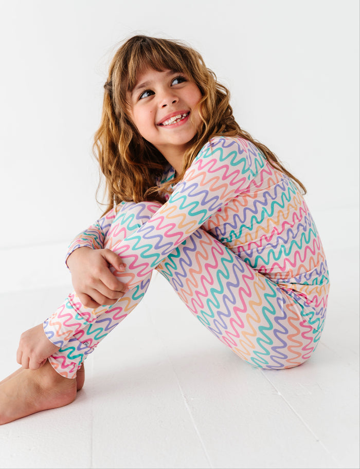Child wearing colorful patterned bamboo pajamas sitting on a white surface