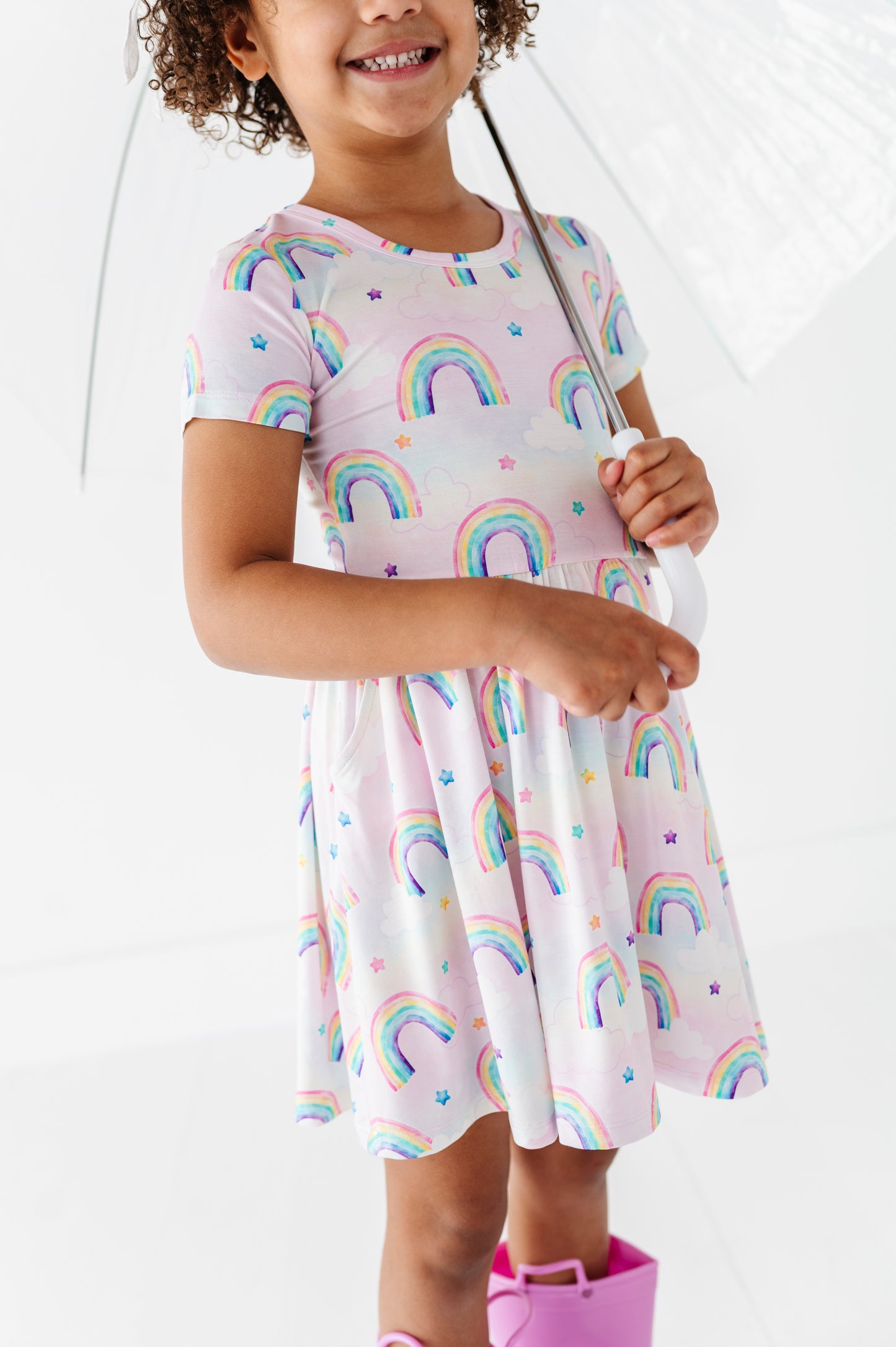 Child wearing a bamboo dress with watercolor rainbow patterns holding a transparent umbrella.
