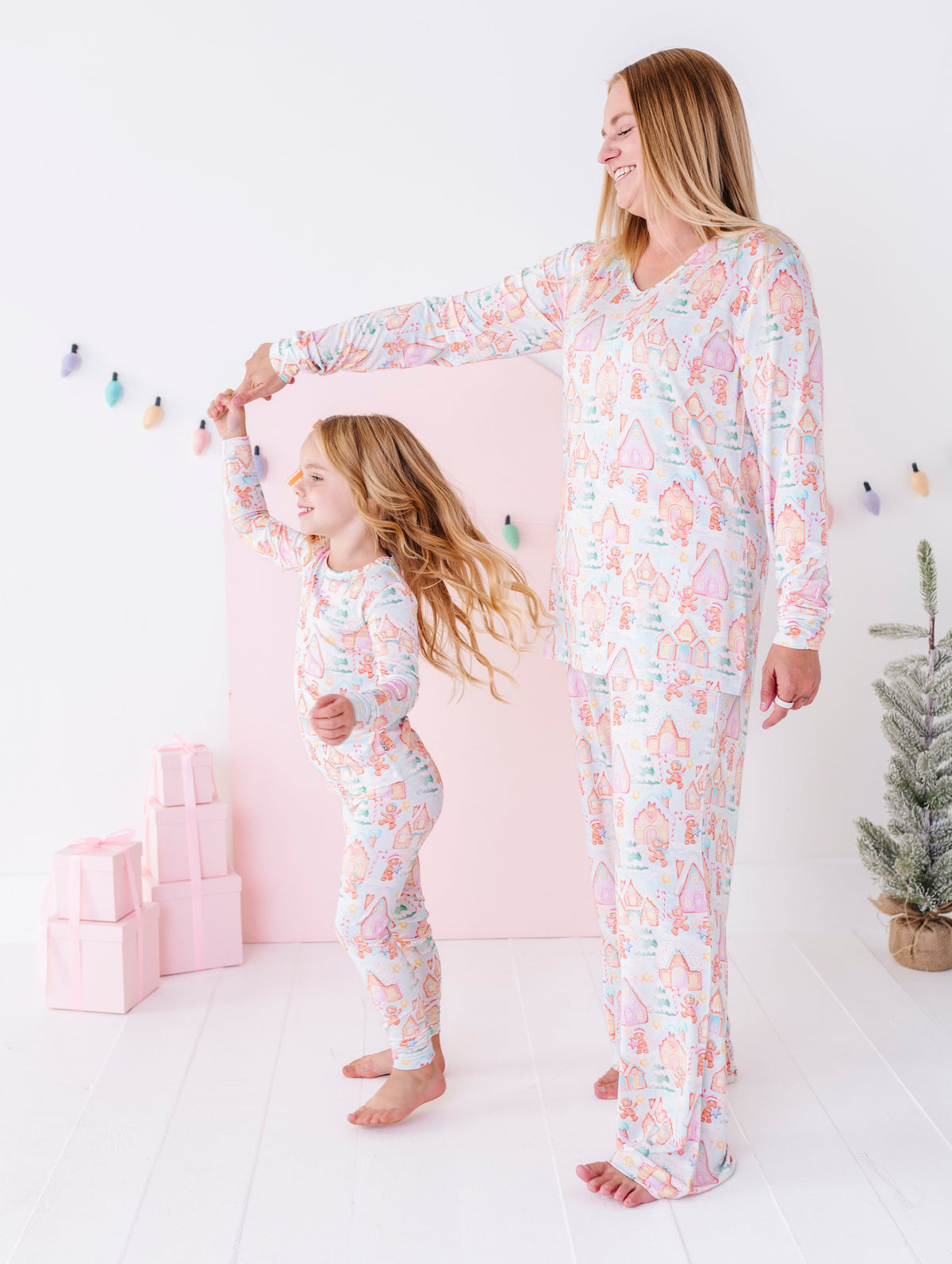 A mom and daughter dancing while wearing matching two-piece bamboo pajama sets featuring gingerbread villages and other Christmas motifs