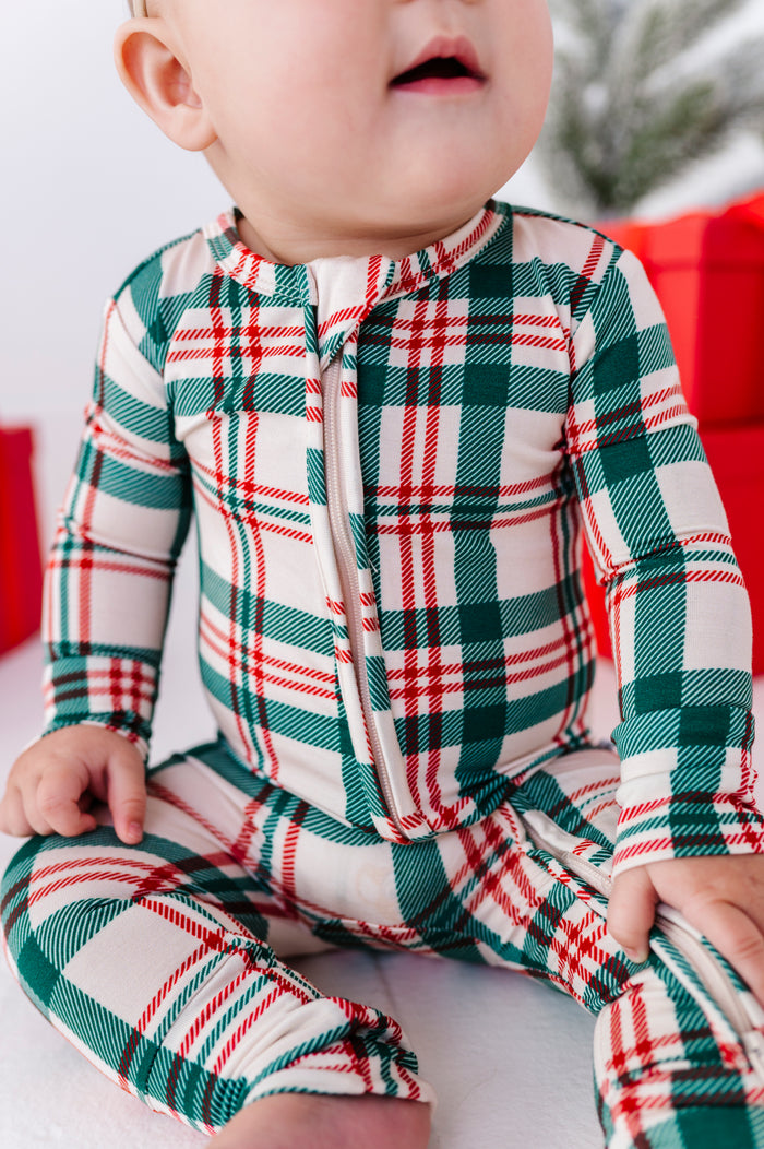 A close-up photo of a baby wearing a red, green, and beige Christmas plaid bamboo convertible romper