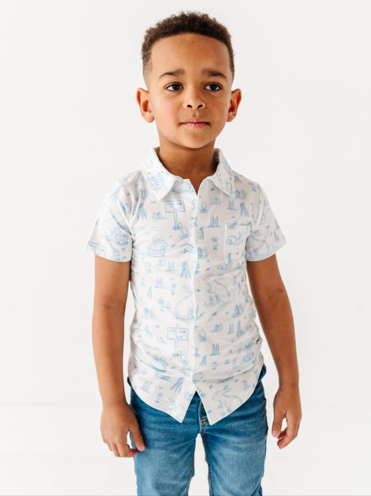 Young boy wearing a white shirt with blue patterns and blue jeans on a white background