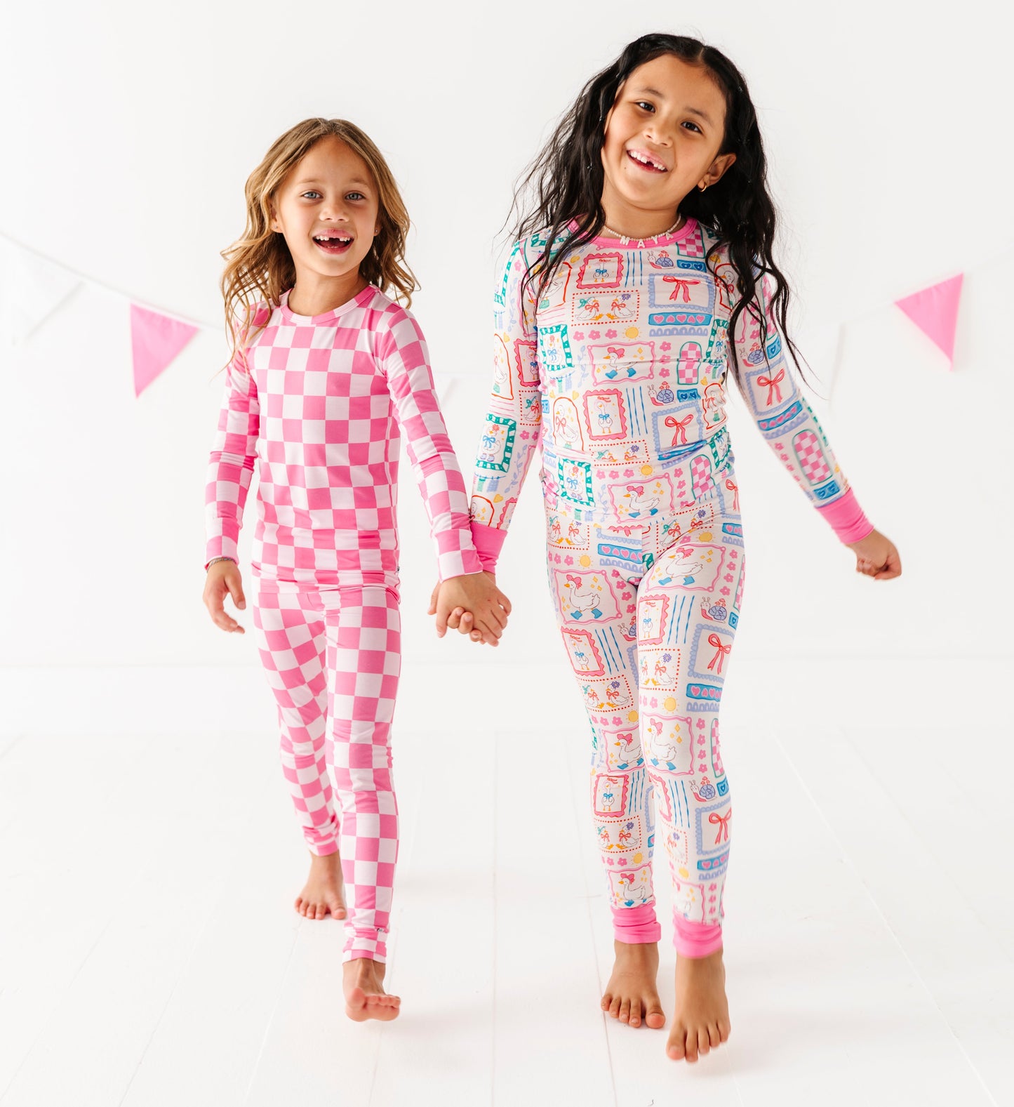 Two children wearing pink and multicolor patterned onesies on a white background