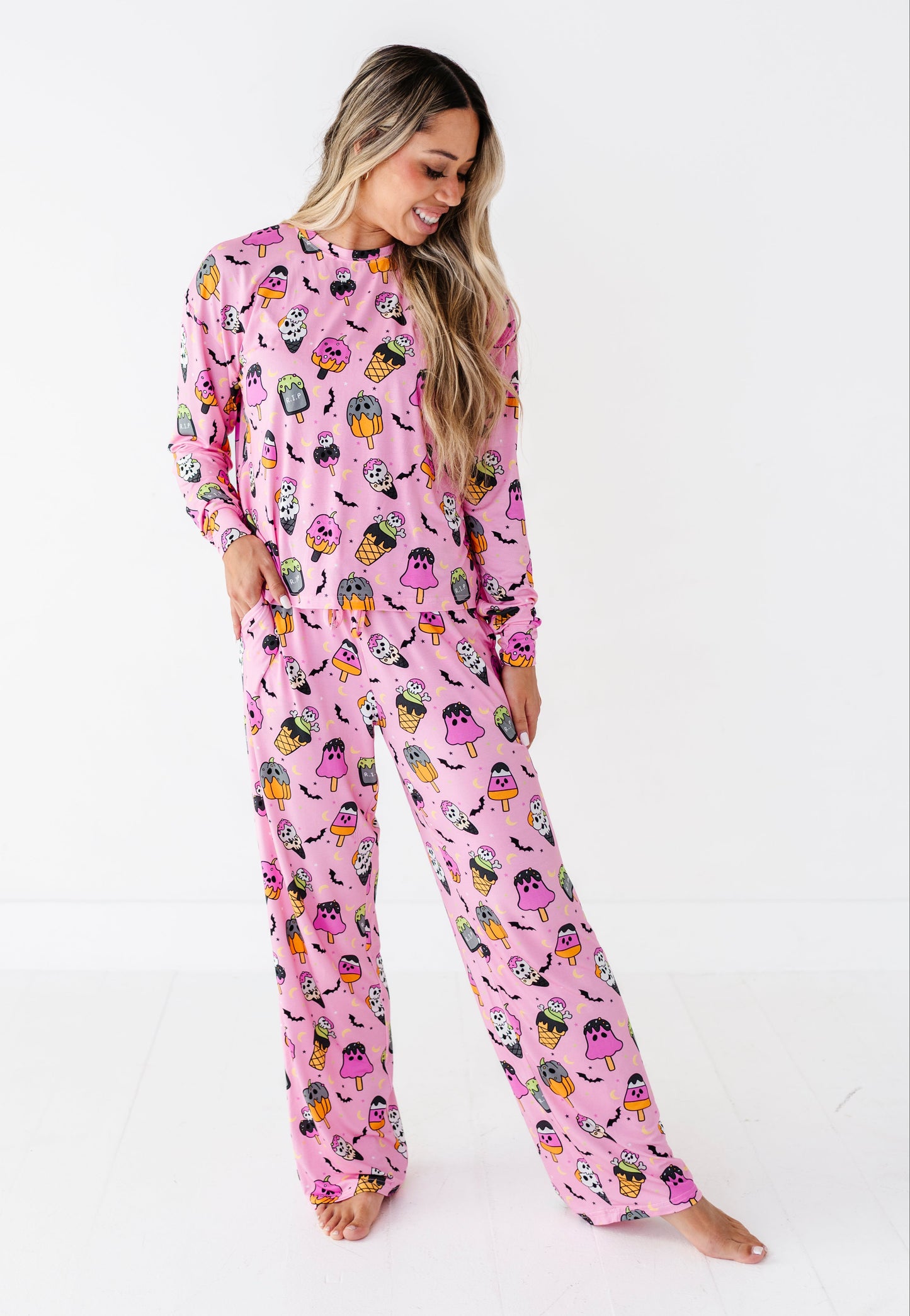 A woman modeling a pink long-sleeve pajama set with a colorful cartoon owl print, standing against a plain white studio background.