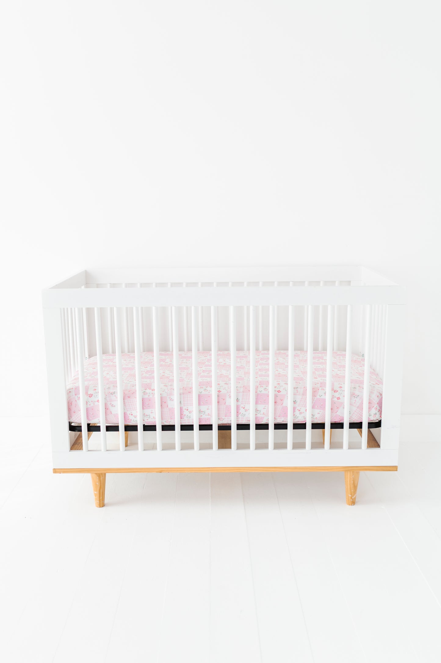 White crib with a pink bamboo crib sheet on a white background