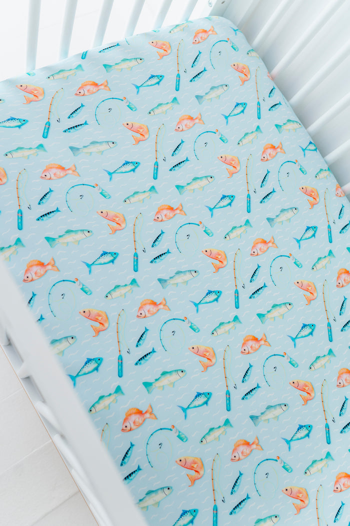 Bamboo crib sheet with fishing-themed pattern on a white crib