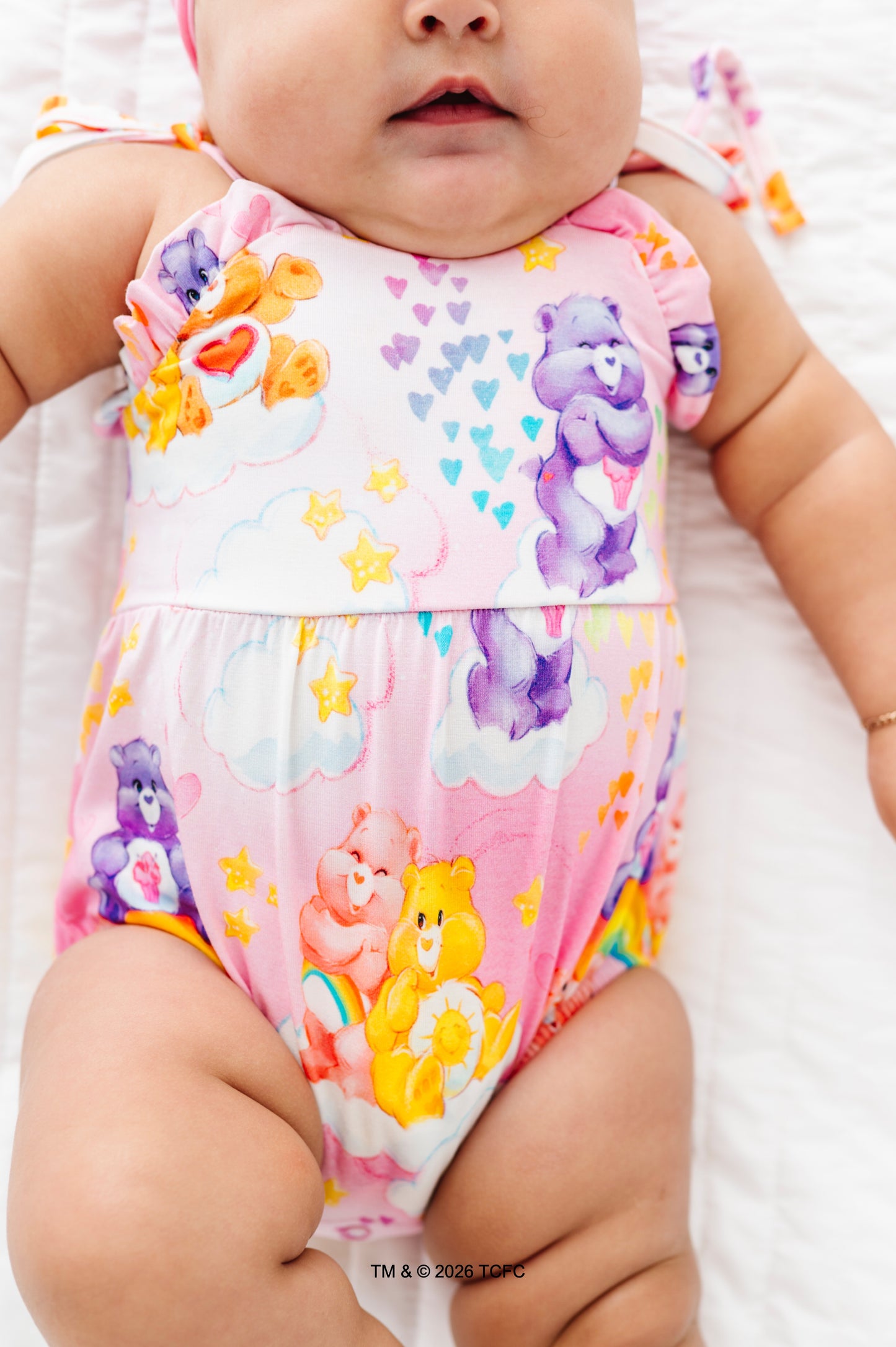 Baby wearing a colorful Care Bears™ bubble romper on a white background