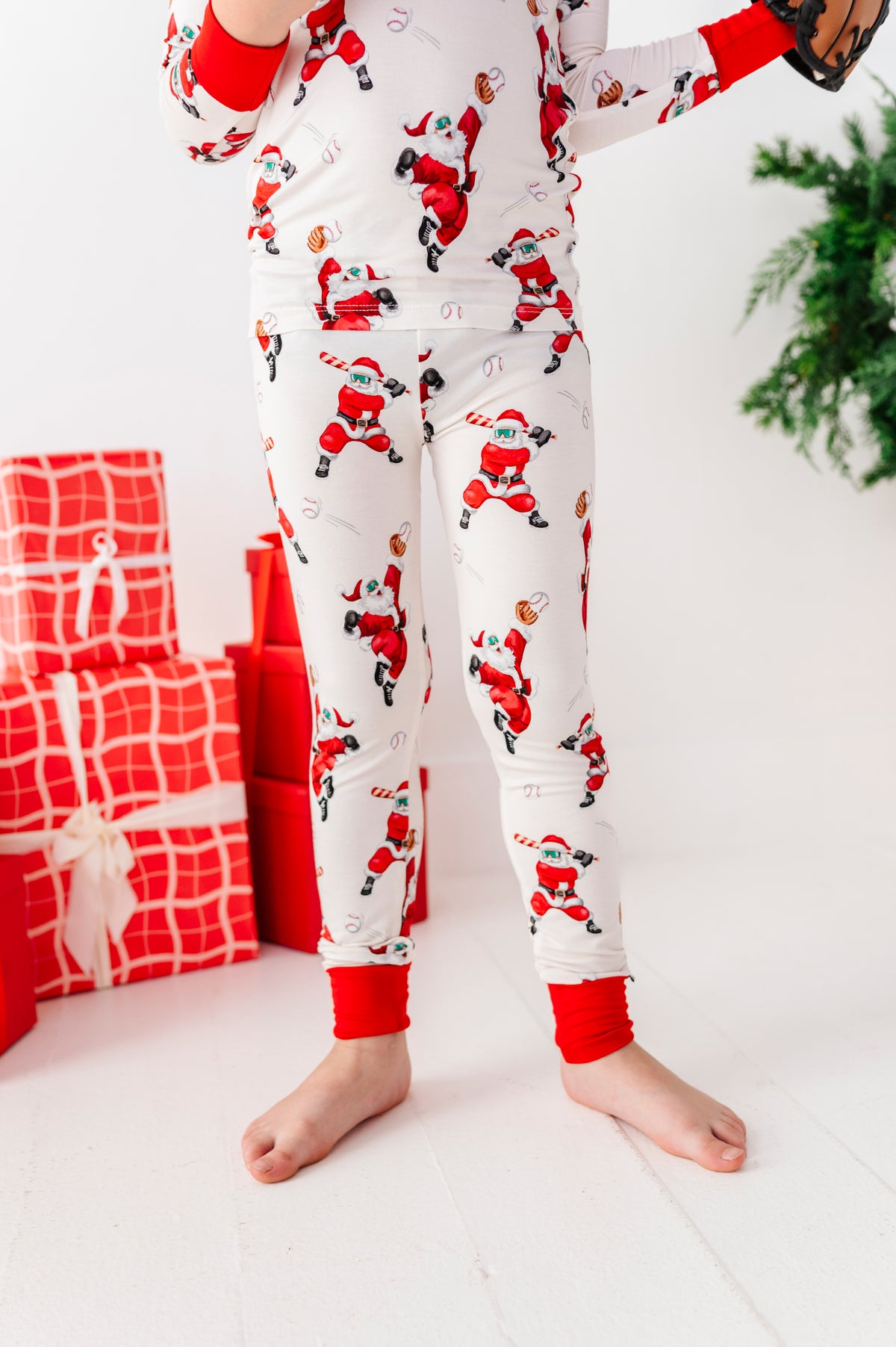 A close-up shot of a bamboo pajama set featuring Santas playing baseball. In the background is a pile of red presents