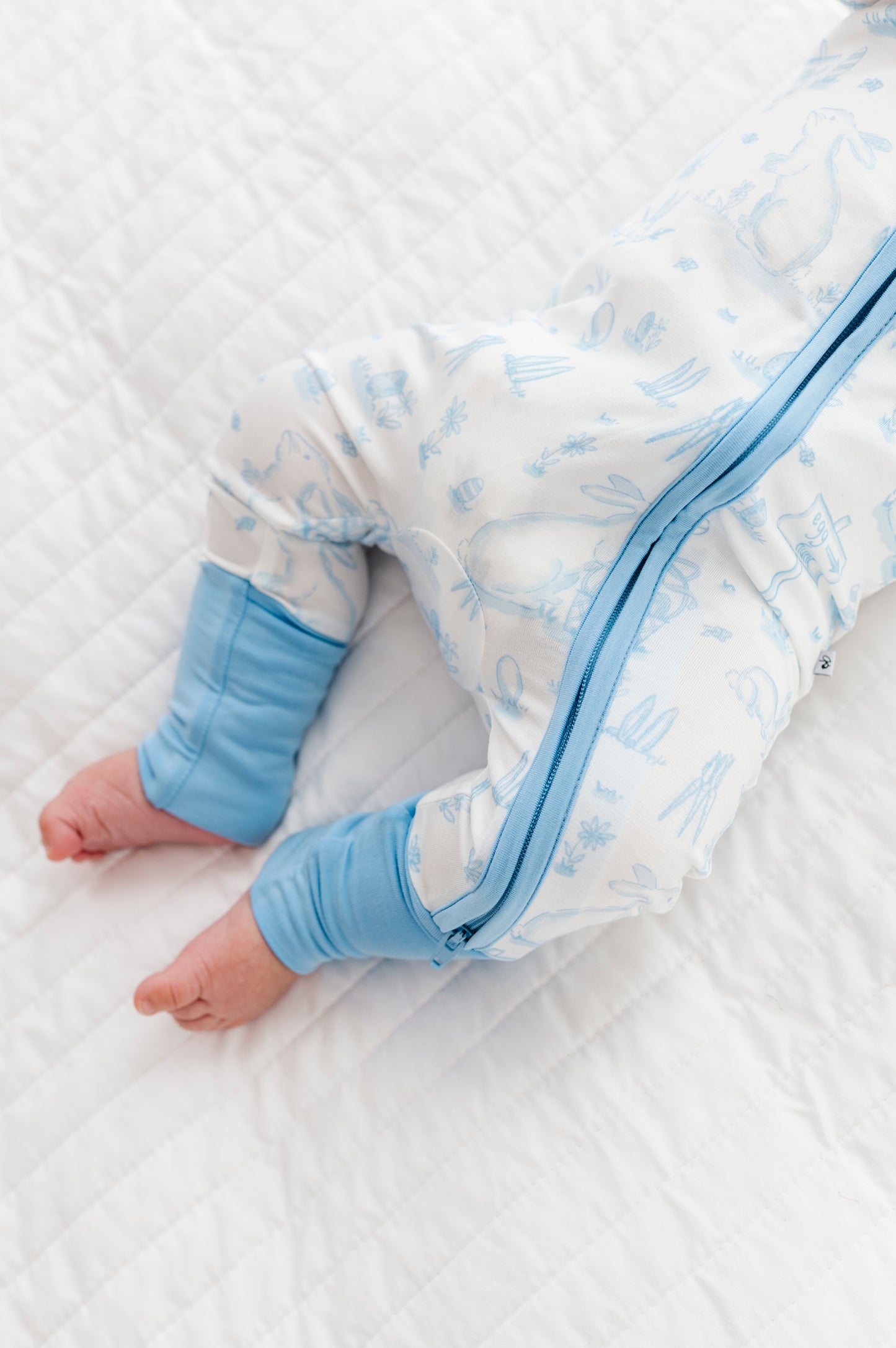 Baby in a white and blue Easter bamboo romper on a white blanket
