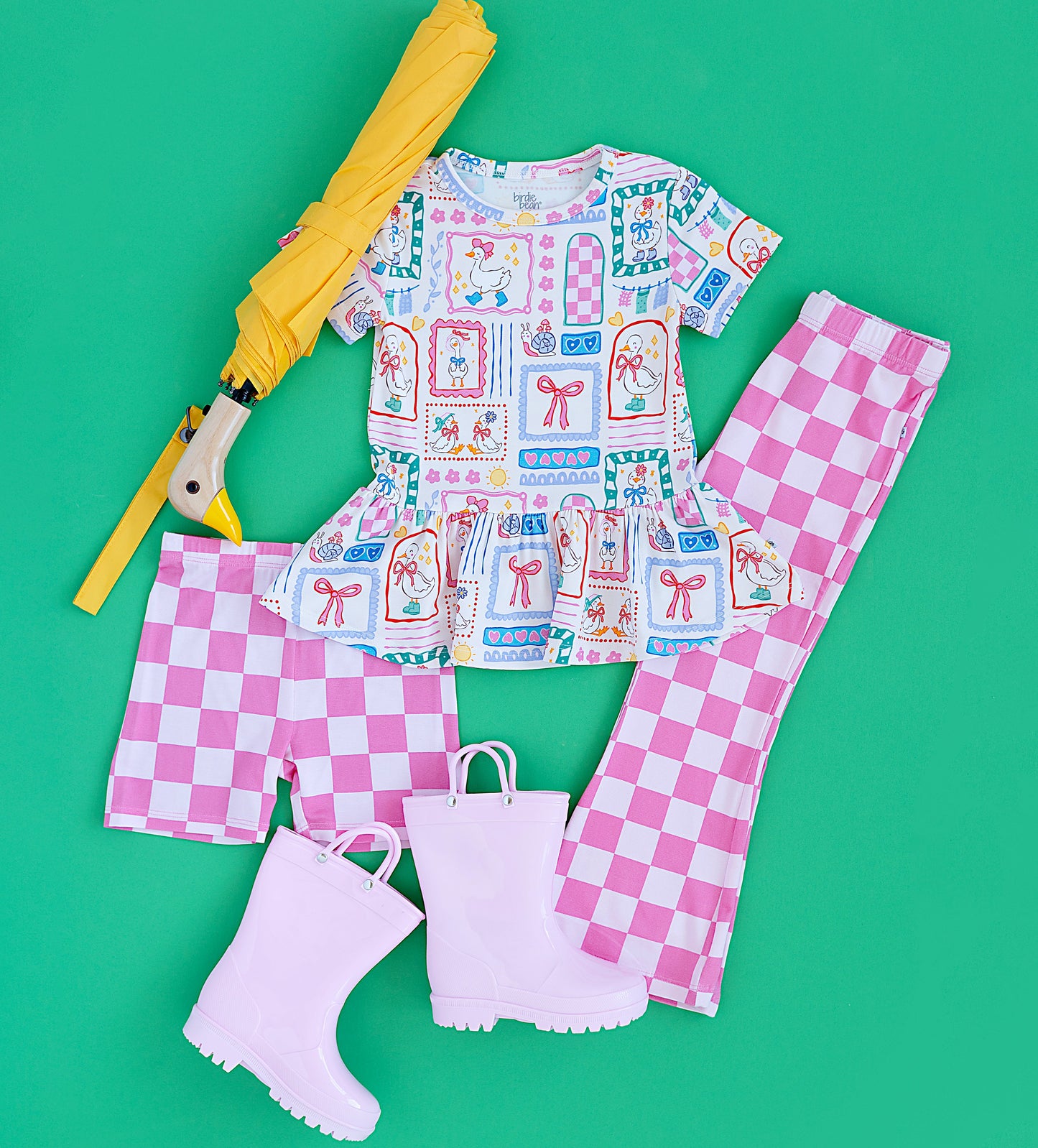 Children's outfit with checkered pants, rain boots, and umbrella on a green background