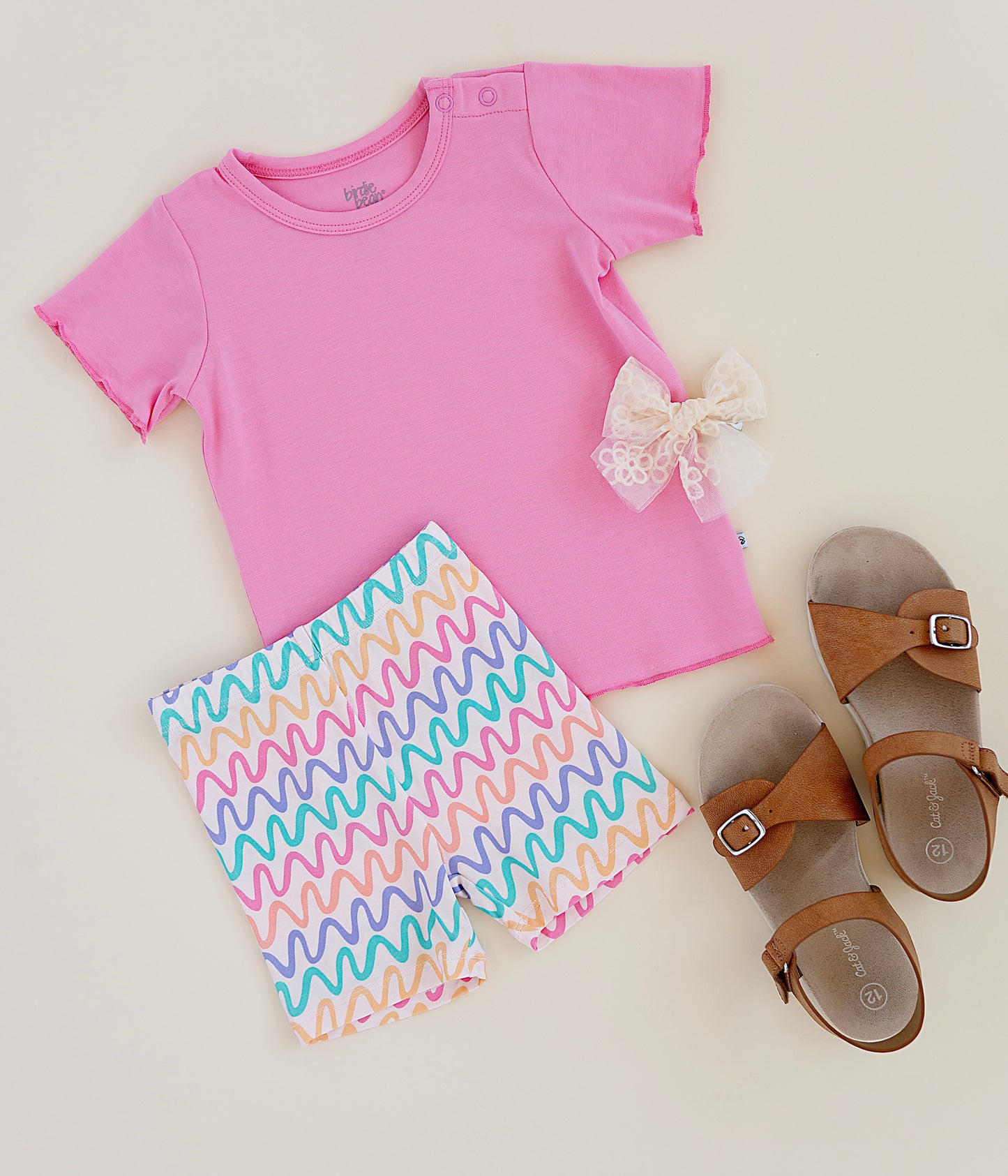 Pink bamboo/cotton top, colorful bamboo biker shorts, and brown sandals on a light background