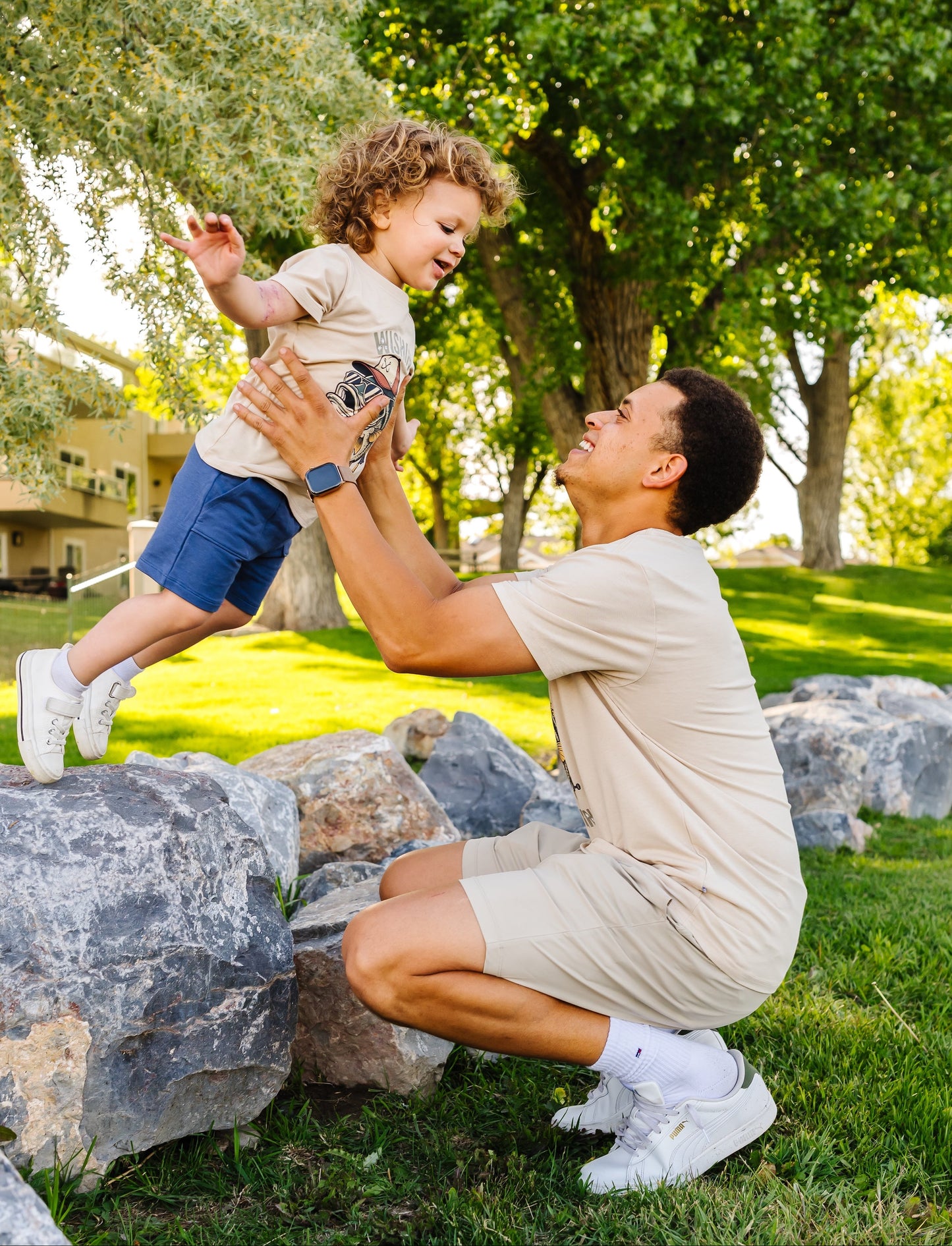 Man playing with a child in a park with trees and rocks in the background