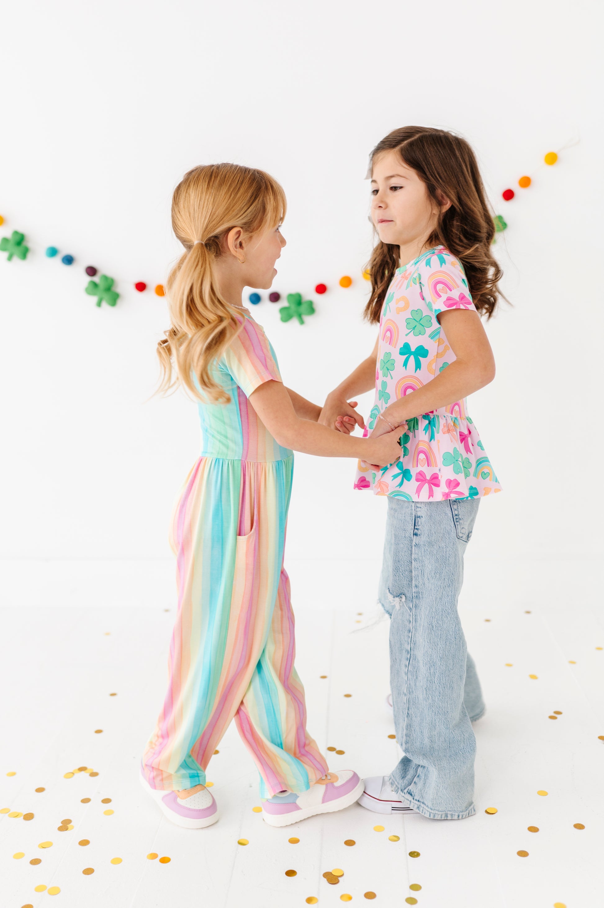 Two young girls standing together with colorful St. Patrick's Day confetti on a white background