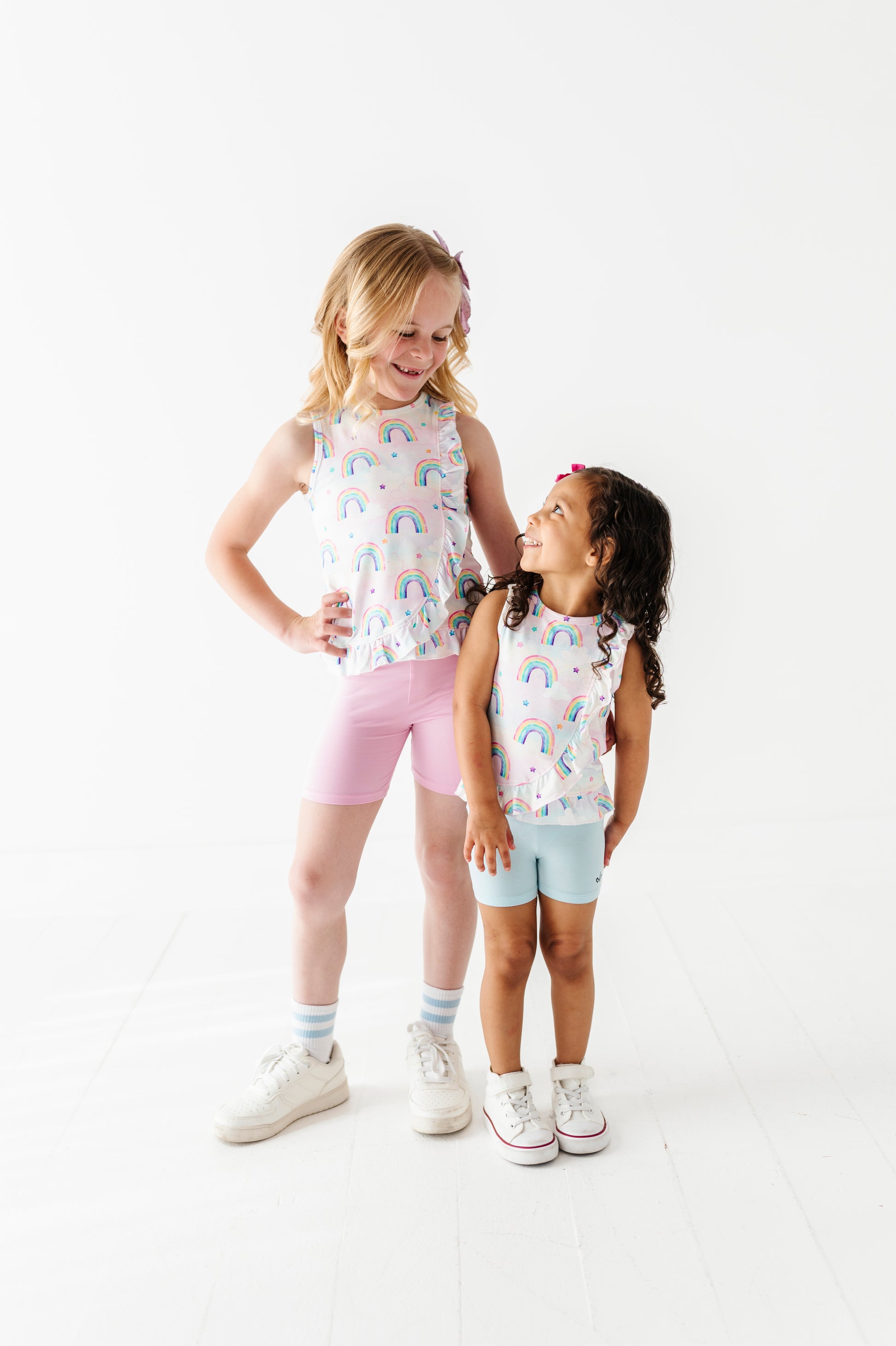 Two young girls wearing matching bamboo outfits with rainbow patterns on a white background